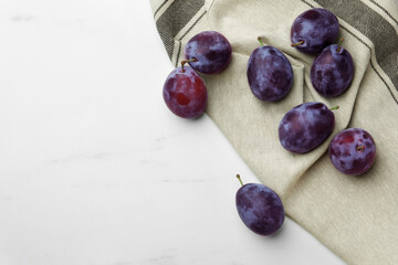Tasty ripe plums on white marble table, flat lay. Space for text