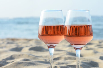 Glasses of tasty rose wine on sand near sea, closeup. Space for text