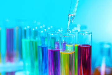 Dripping liquid from pipette into test tube on light blue background, closeup