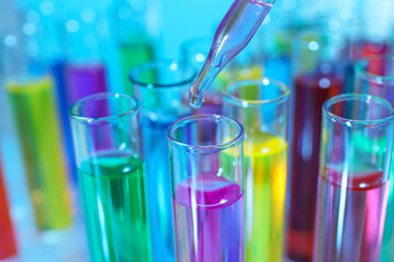 Dripping liquid from pipette into test tube on light blue background, closeup