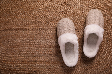 Fototapeta na wymiar Pair of warm stylish slippers on wicker carpet, top view. Space for text