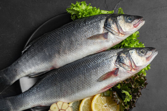 Fresh Raw Sea Bass Fish And Ingredients On Black Table, Top View