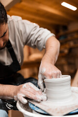 Man hands working on pottery wheel and making a pot.