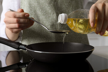 Woman with spoon pouring cooking oil into frying pan on stove, closeup