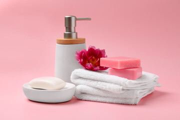 Fototapeta na wymiar Soap bars, bottle dispenser and towels on pink background