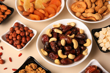 Bowls with dried fruits and nuts on beige background