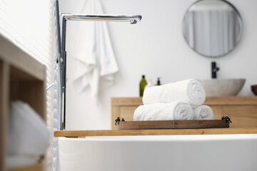 Rolled bath towels on tub tray in bathroom