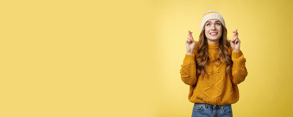 Nervous cute optimistic hopeful young attractive stylish woman praying god make wish look sky faithfully smiling cross fingers good luck wanna fulfill dream, standing anticipating yellow background - obrazy, fototapety, plakaty