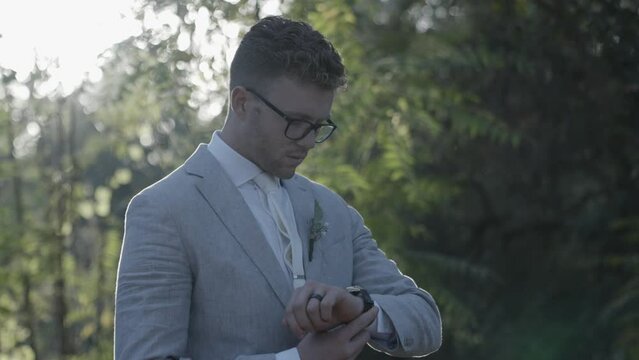 Groom adjusts his tie and watch then looks at camera with sun in the background. 4k60 fps. Email willneatheryyahoo.com to purchase entire wedding event at cheap wholesale price.