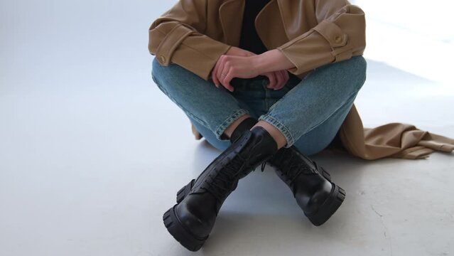 Black combat ankle boots on tractor soles with laces. Close up. Female model in jeans and coat demonstrates warm footwear.