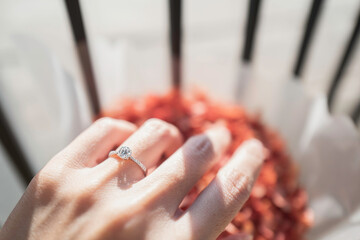 Close up of diamond ring on woman’s finger while touching flower with sunlight and shadow background. Love, valentine, relationship and wedding concept. Soft and selective focus.