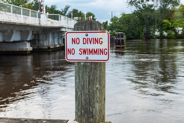Wooden pole with "No swiming sign" on the river near the bridge.