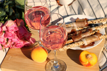 Glasses of delicious rose wine, flowers and food on white picnic blanket, closeup