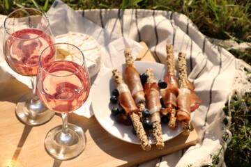 Glasses of delicious rose wine and food on picnic blanket outdoors