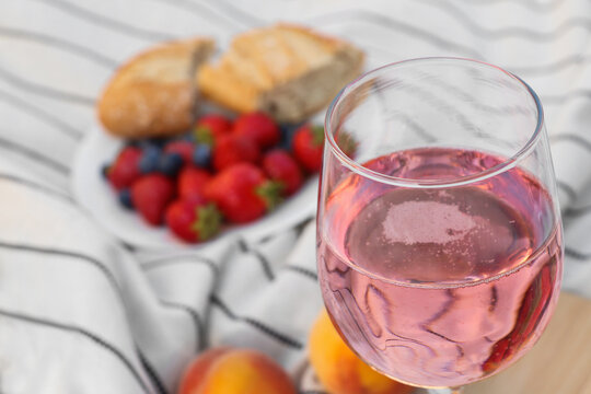 Glass of delicious rose wine and food on white picnic blanket, closeup