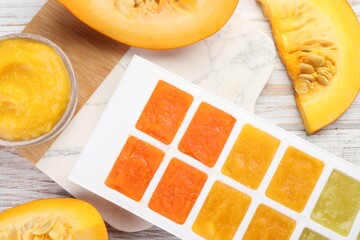 Different purees in ice cube tray and fresh pumpkin on white wooden table, flat lay. Ready for...