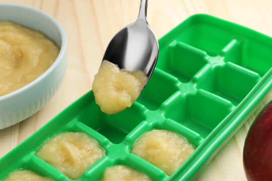 Putting apple puree ice cube tray on wooden table, closeup. Ready for freezing
