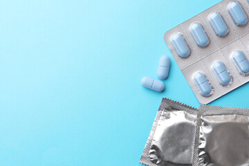 Pills and condoms on light blue background, flat lay with space for text. Potency problem