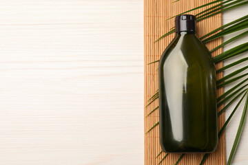 Shampoo bottle, bamboo mat and green leaf on white wooden table, flat lay. Space for text