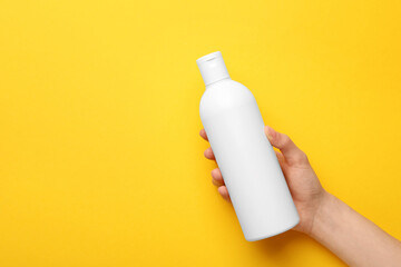 Woman holding shampoo bottle on yellow background, top view. Space for text