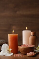 Beautiful spa composition with sea salt, burning candles and flowers on wooden table