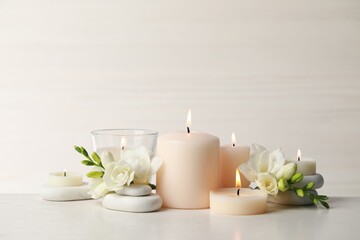 Fototapeta na wymiar Beautiful composition with burning candles, spa stones and flowers on white table. Space for text