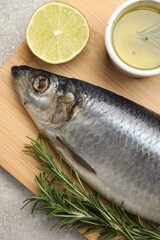 Wooden board with salted herring, lime, oil and rosemary on grey table, top view