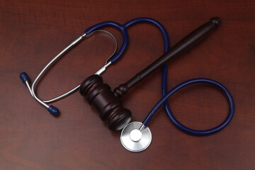 Wooden judge gavel and stethoscope on table. Malpractice and crimes concept.
