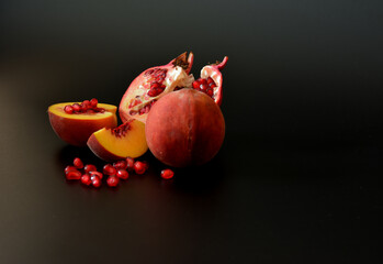 Pieces of a ripe peach and a broken pomegranate with a scattering of seeds on a black background.