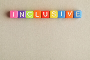 Colorful cubes with word Inclusive on beige background, flat lay. Space for text