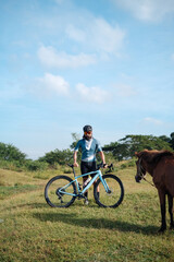 Obraz premium A young bearded cyclist is biking through a field with a horse