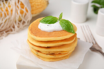 Tasty corn pancakes with sauce and basil on white table, closeup