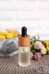 Glass bottle of essential oil, mortar with pestle and different wildflowers on wicker mat