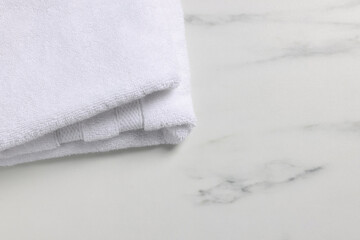 Fototapeta na wymiar Clean folded towel on white marble table, space for text