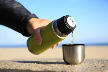 Woman pouring hot drink from yellow thermos into cap on stone surface outdoors, closeup