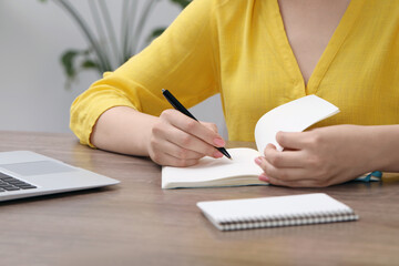 Woman writing in notebook at wooden table indoors, closeup