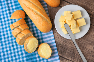 Tasty cut baguette with fresh butter on wooden table, flat lay