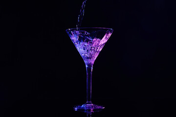 Pouring martini into glass in neon lights on dark background
