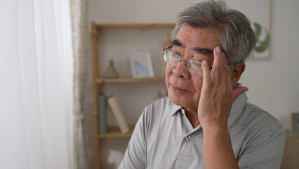 thoughtful middle aged Korean mature grandfather standing by window looking away. Pondering asian old senior hoary man think of psychological health problems spend time alone at home