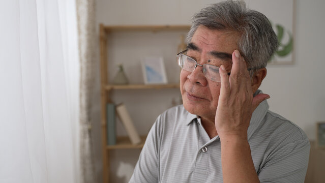 Thoughtful Middle Aged Korean Mature Grandfather Standing By Window Looking Away. Pondering Asian Old Senior Hoary Man Think Of Psychological Health Problems Spend Time Alone At Home