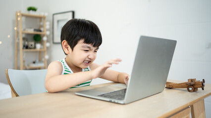 Asian young Little boy addicted playing video game on laptop at home. alone playing tablet computer...