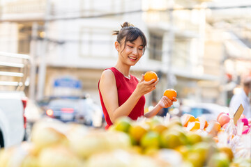 Portrait of Attractive Asian woman holding shopping bag choosing and buying orange fruit at Bangkok...