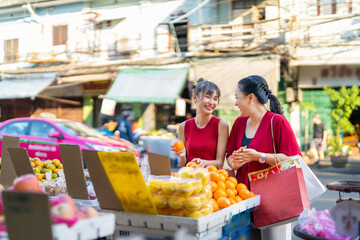 Happy Asian family mother and daughter choosing and buying fresh fruit orange together at Bangkok Chinatown street market for celebrating Chinese Lunar New Year festive. Chinese culture concept.