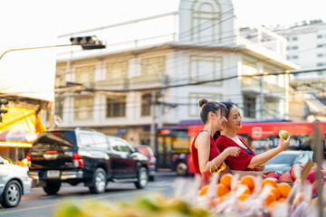 Happy Asian family mother and daughter choosing and buying fresh fruit orange together at Bangkok Chinatown street market for celebrating Chinese Lunar New Year festive. Chinese culture concept.