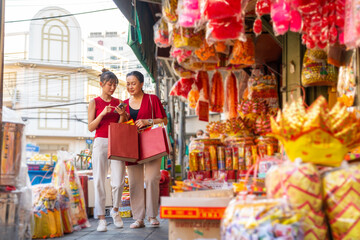 Asian mother and daughter using navigator on mobile phone while shopping home decorative ornaments and joss paper for celebrating Chinese Lunar New Year festival together at Chinatown street market.