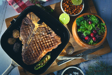 Grilled t-bone or porterhouse steak seasoned with rosemary in a grill pan with salad