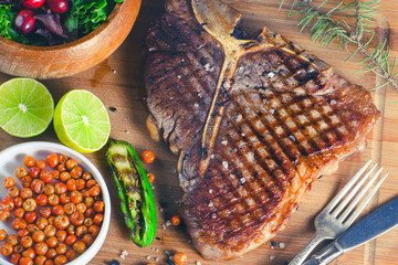 Grilled t-bone or porterhouse steak seasoned with rosemary in a rustic kitchen on a wooden board with jalapeño