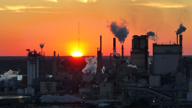 Huge factory with high chimneys polluting atmosphere with carbon dioxide smoke from production process at plant manufacturing yard. Industrial site at sunset