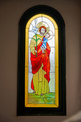 stained glass window of the church with the image of St. Joseph and baby Jesus. religious image of a robed man holding a child in the window of the church. artwork painted on a window of the chapel. 