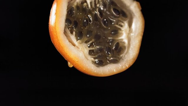 Slow Motion Macro Shot of Flowing Granadilla Juice from Halved Granadilla in black Background